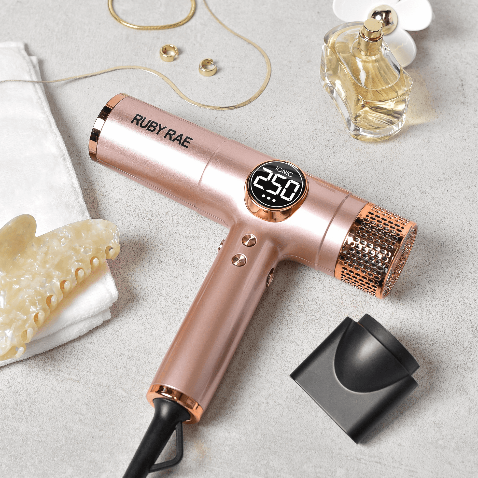 Rose gold hair dryer with digital display on a light gray surface, surrounded by beauty products.